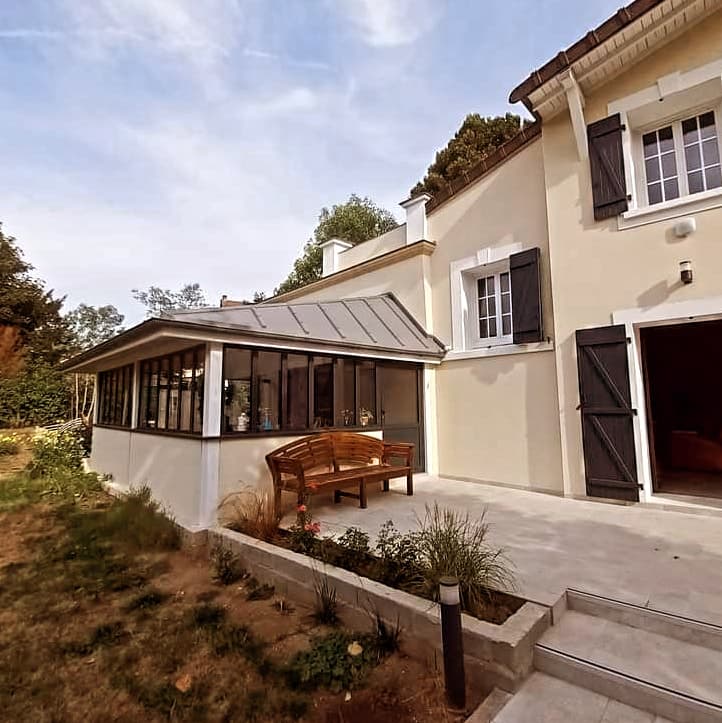 Extension vitrée à Montmorency accolée à la maison existante, avec terrasse et marches vers le jardin.