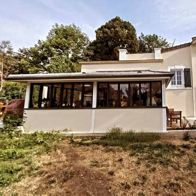 Façade de l’extension à Montmorency, grandes baies aux montants foncés et soubassement clair, vue depuis le jardin.