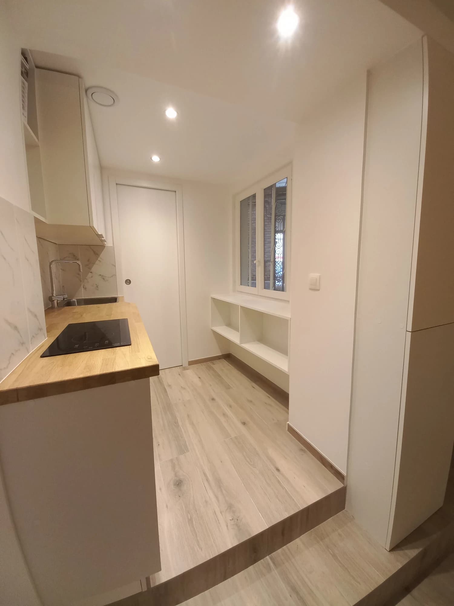 Cuisine linéaire de l’appartement parisien, avec meubles blancs et plan de travail en bois.