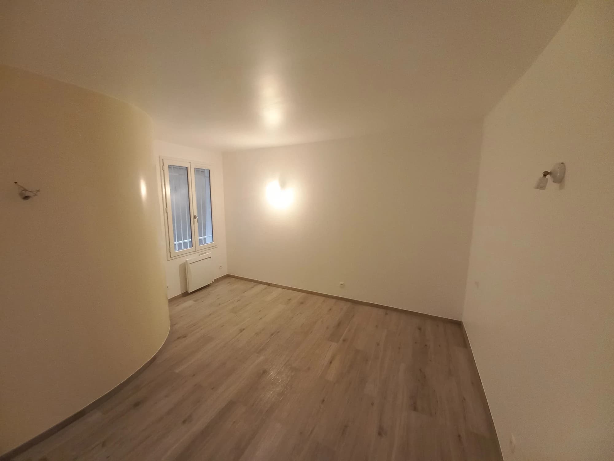 Pièce principale de l’appartement parisien avec paroi courbe, fenêtre et éclairage au plafond.