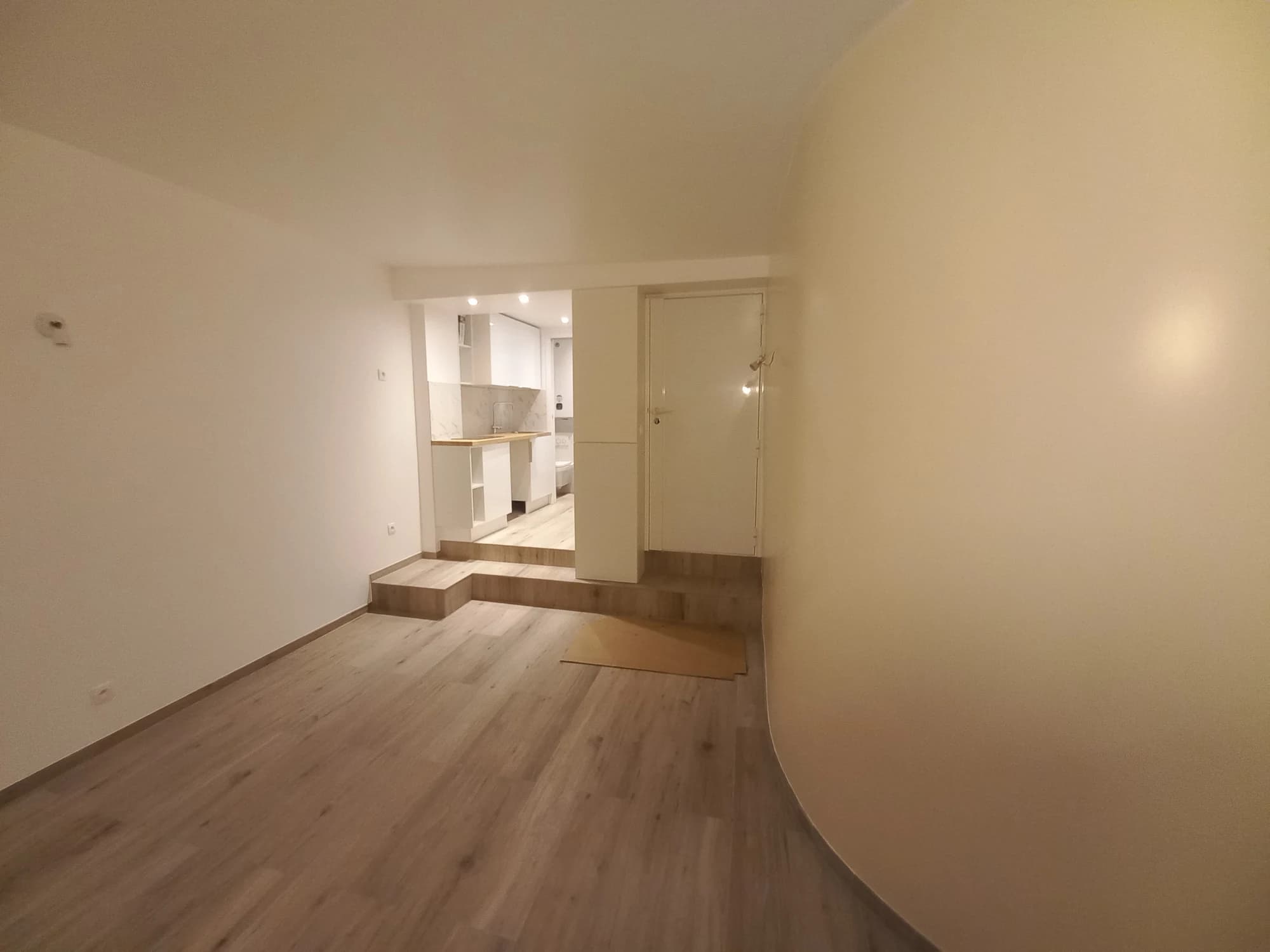 Pièce principale d’un appartement parisien, avec sol clair, paroi courbe et cuisine en retrait.