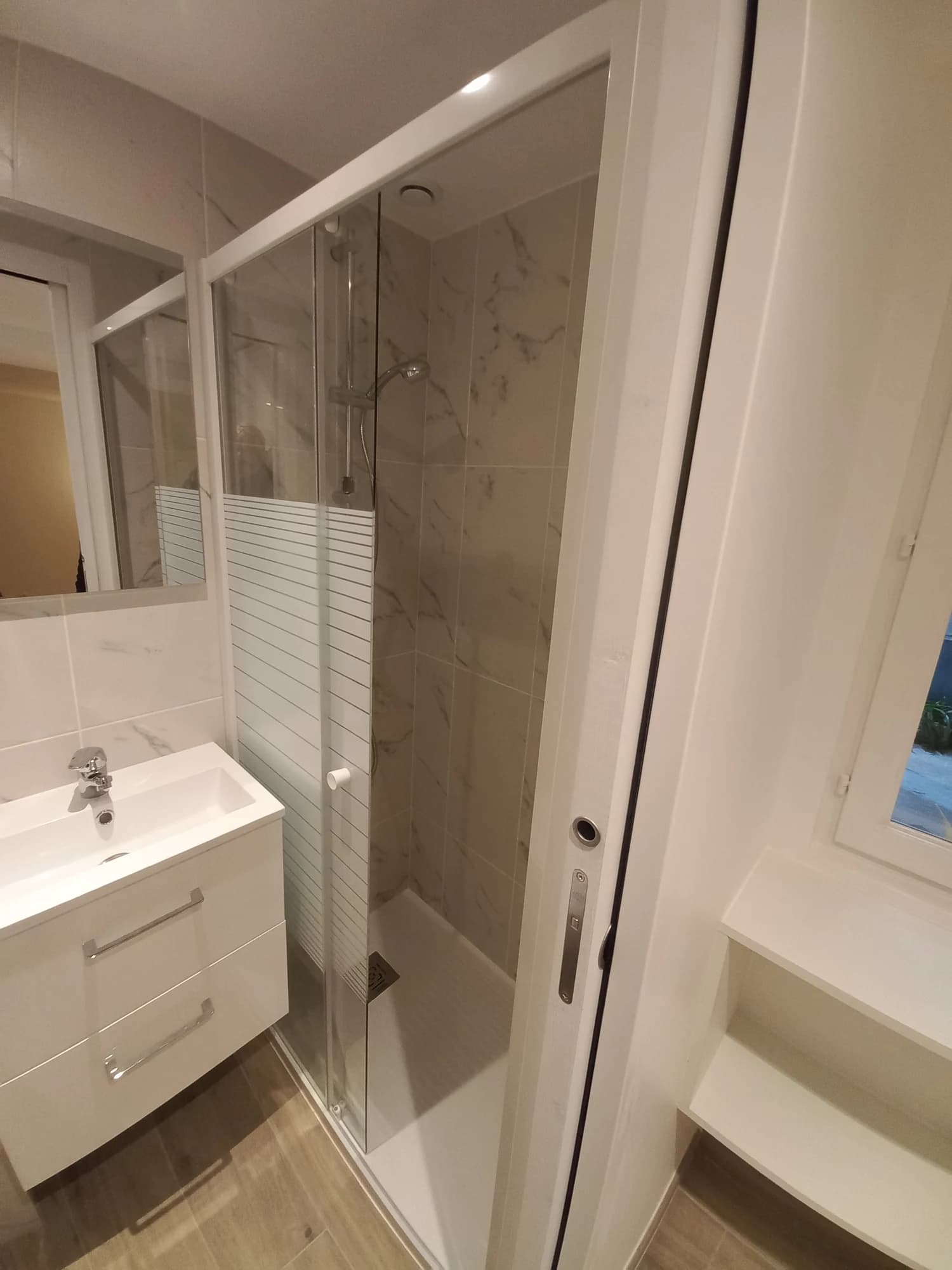 Salle d’eau de l’appartement parisien avec douche vitrée, meuble vasque et revêtement mural clair.