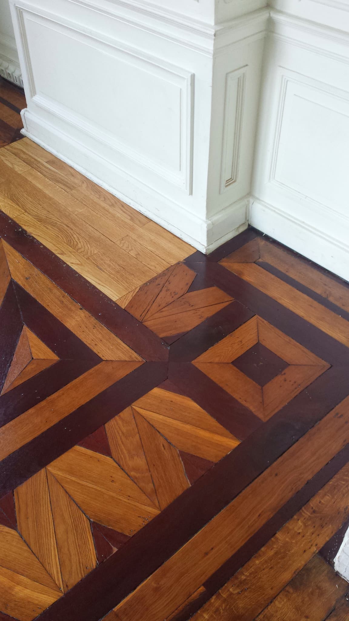 Détail de parquet géométrique au pied de boiseries blanches.