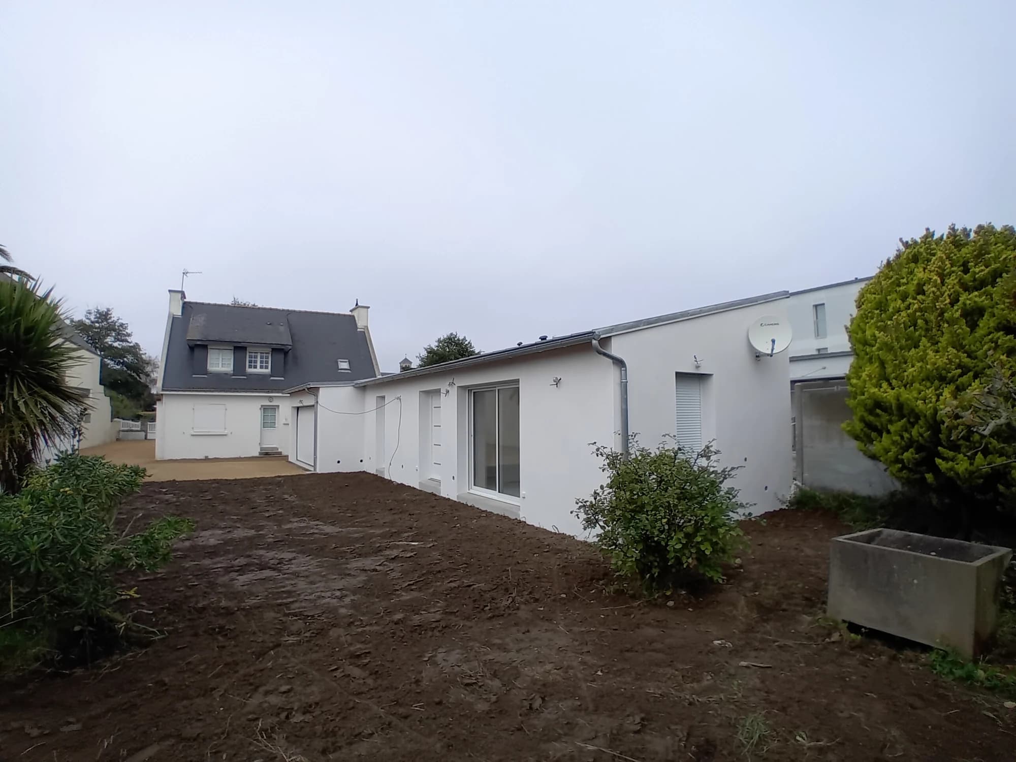 Façade blanche de l’extension à Quiberon, ponctuée de baies donnant sur les abords.