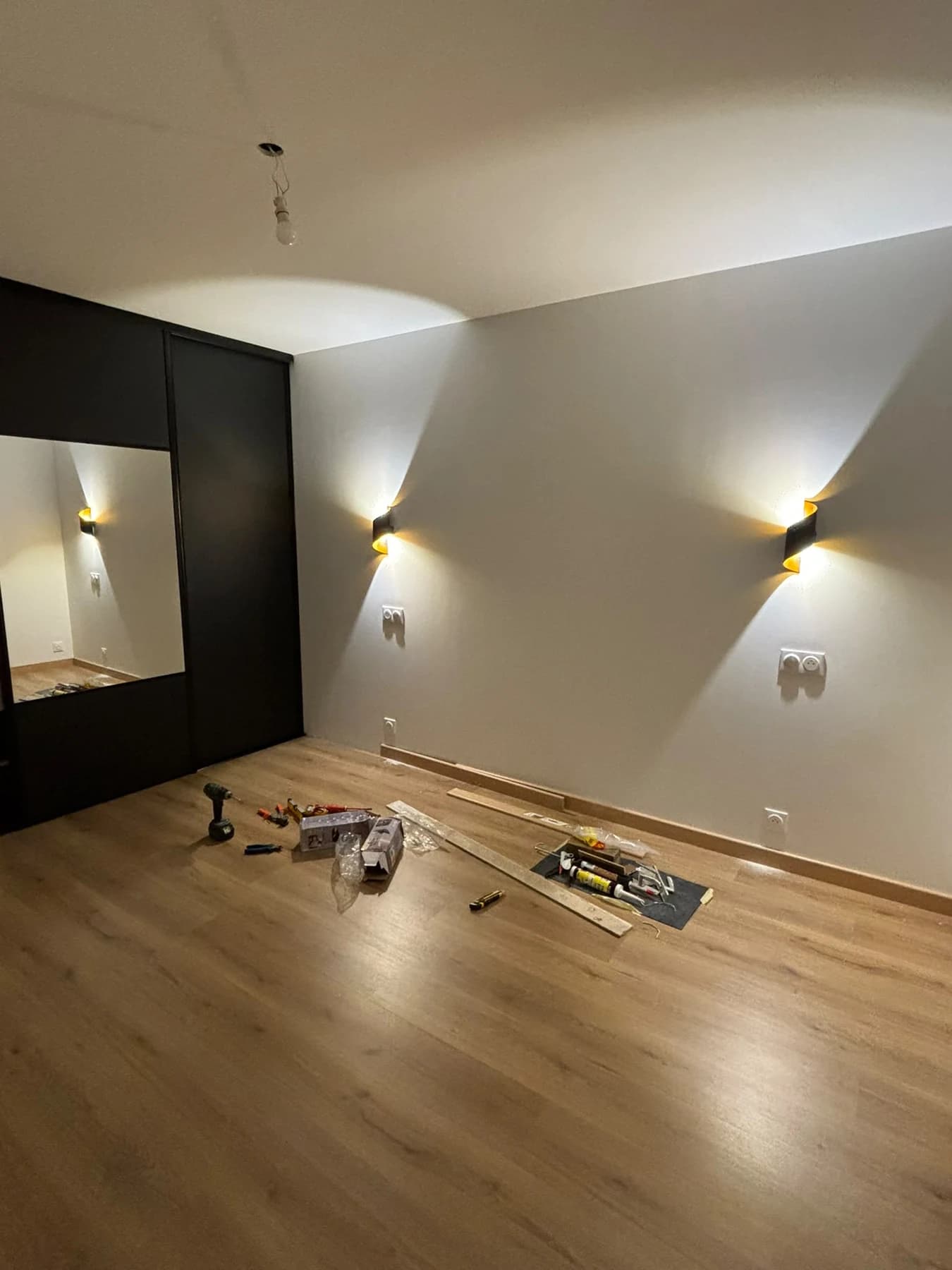 Chambre rénovée avec sol de teinte bois, appliques murales et placard sombre.