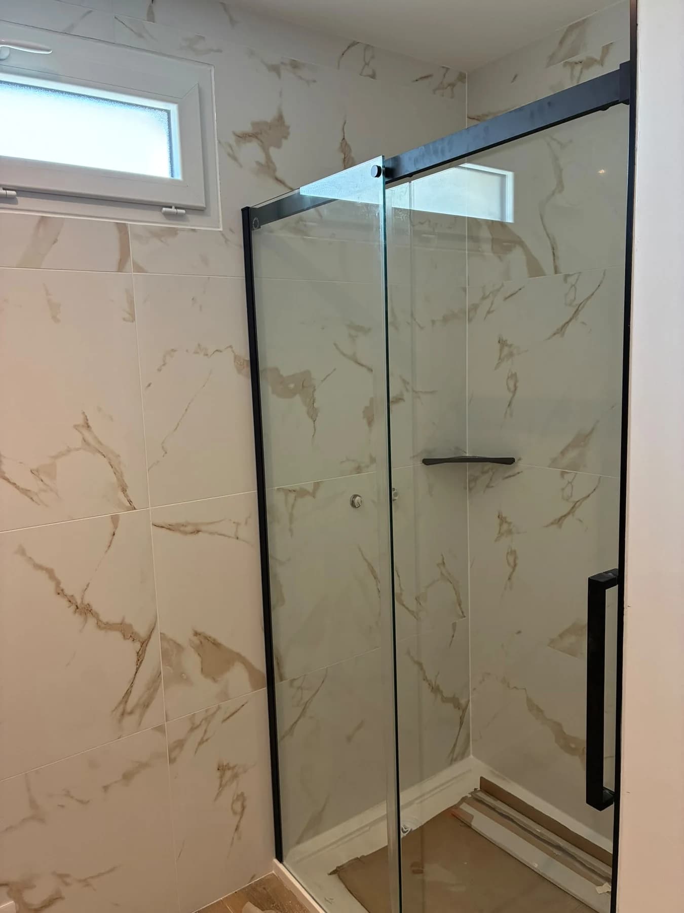 Douche avec paroi vitrée et revêtement clair veiné à Soisy-sous-Montmorency.