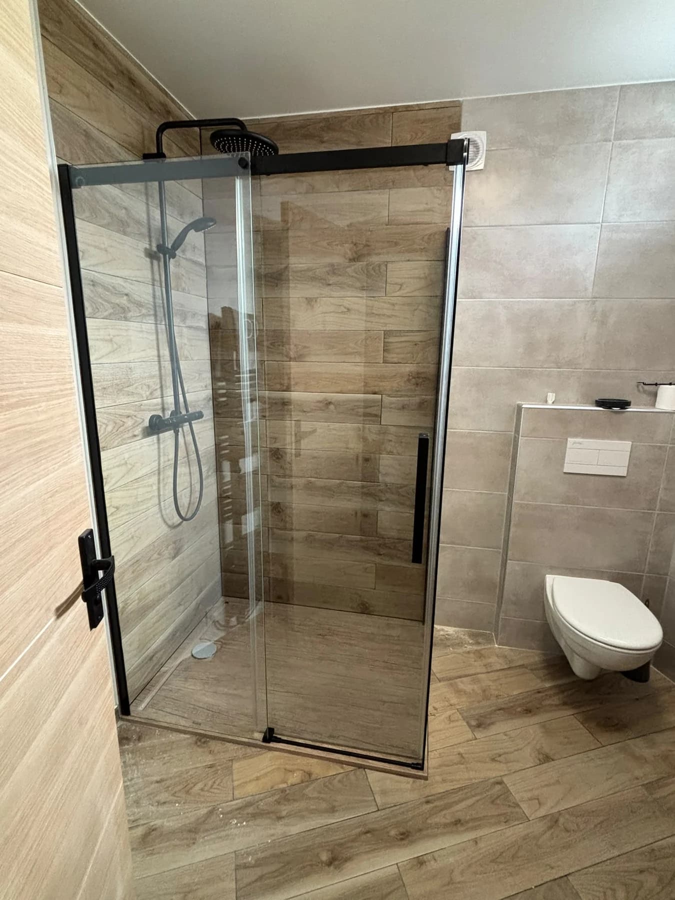 Salle d’eau rénovée avec douche vitrée, revêtement de teinte bois et sanitaires.